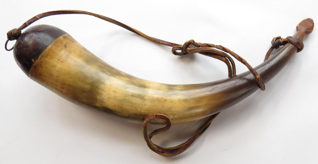 AN AMERICAN POWDERHORN: Polished horn with hemispherical hardwood cap and flared aperture. With original stopper, lanyard a working life Replacement. 19th century. Worn. Overall length 38.5cm. Condition III