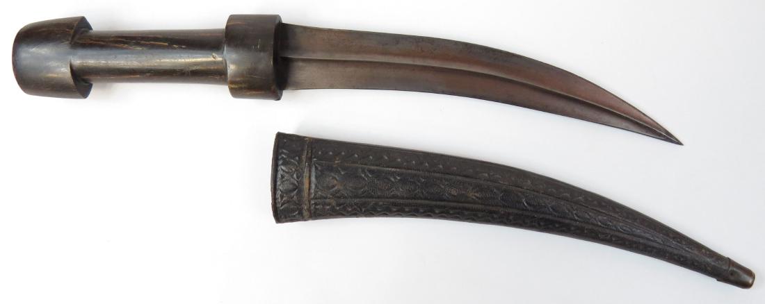A KURDISH DAGGER: The grip of typical form, carved of a single large section of horn, the heavy blade wrought of fine black wootz, lightly curved and double-edged, with central ridge. The leather-covered wooden scabbar