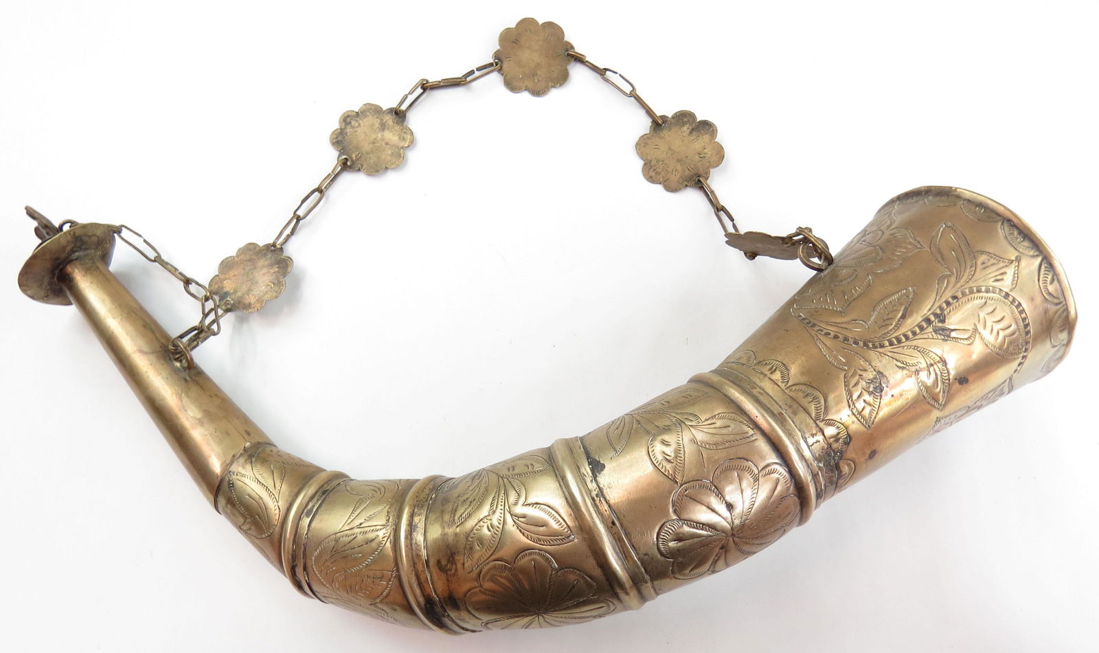 A SPANISH COLONIAL POWDERHORN: Mexican work, the white metal body of segmented construction embellished with extensive foliate engraving, the cap with a rising eagle finial. Retains its suspension chain with scalloped medallions. L