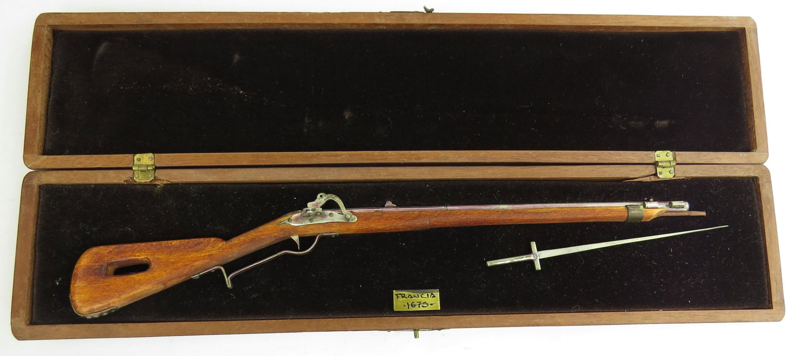 A FINE MINIATURE MATCHLOCK MUSKET BY EDUARDO RUIZ: A miniature matchlock musket with plug bayonet made entirely by hand, the stock carved of hardwood with percussion mechanism, barrel, triggerguard and appliques all superbly detailed in metal. In its 