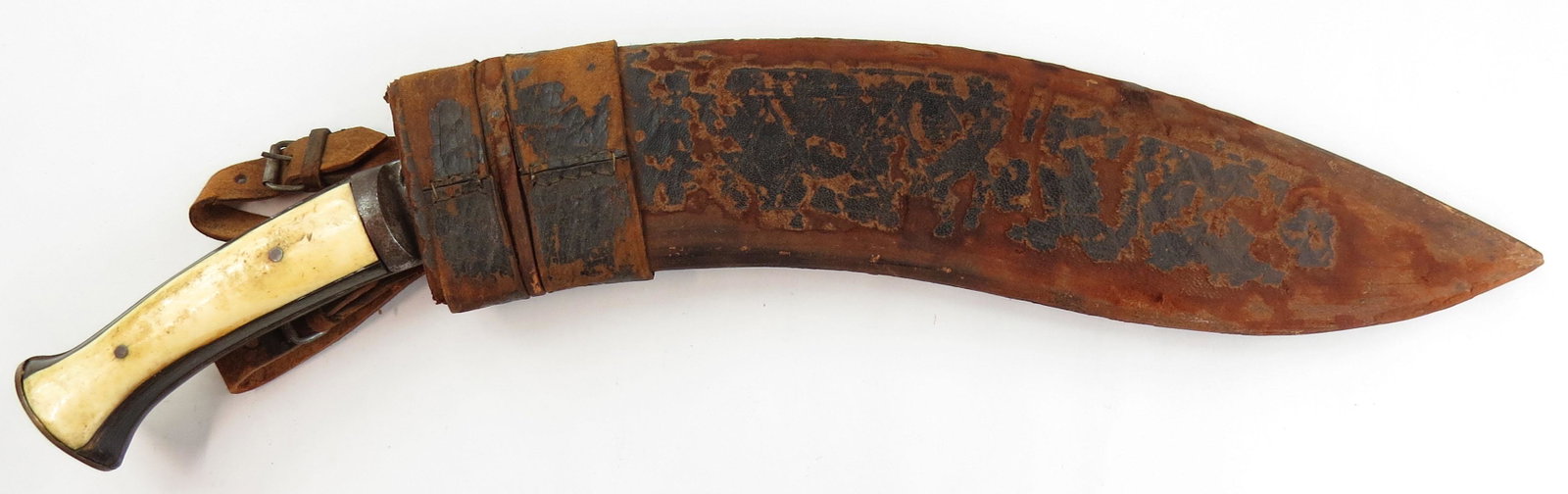 A NEPALESE KUKRIE DAGGER: A massive example, with horn and elephant grips and steel bolsters, the thick, sharp blade with characteristic choil and chamfered cutting edge. In its leather-covered wooden scabbard. Early 20th cent