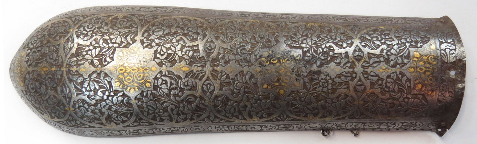 A PERSIAN BAZUBAND ARMGUARD ARMOR: Early Qajar Dynasty, raised from a single plate and finely chiseled overall in flowering vinework with gold embellishments. Early 19th century. Overall length 30.2cm. Condition II