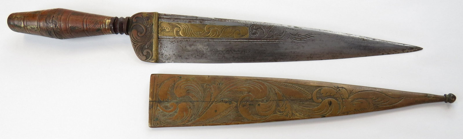 A MEDITERANNEAN DAGGER: Likely Spanish, the grip of plug-form mounted in engraved brass with large bolster. Broad, single-edged engraved blade with substantial backedge and an inlaid and engraved brass panel. Brass sheath en