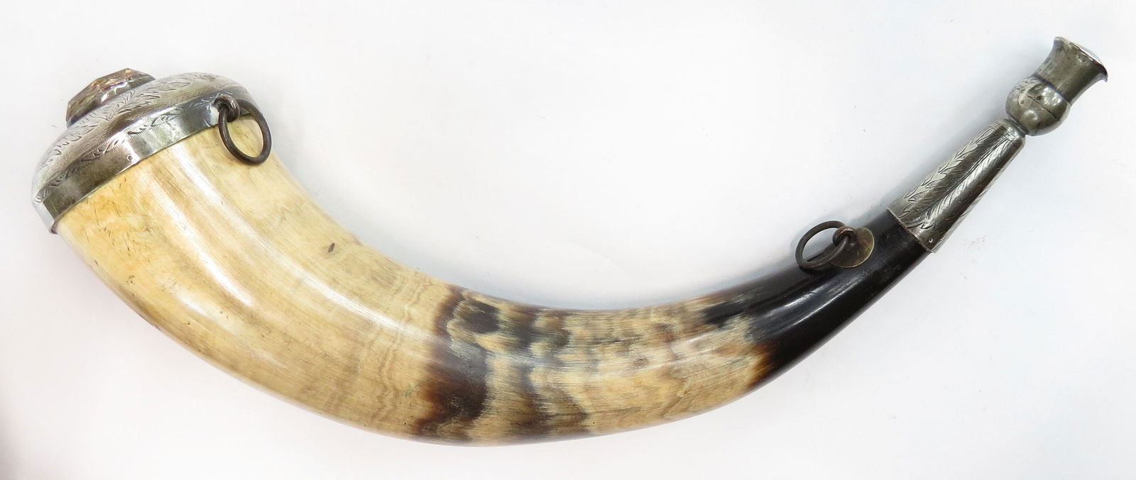 A SCOTTISH POWDERHORN: The polished horn body mounted in silver, engraved in vinework with thistles, the cap set with a glass gem, the spout with thistle-form terminal. Minor wear overall. First half of the 19th century. Ov