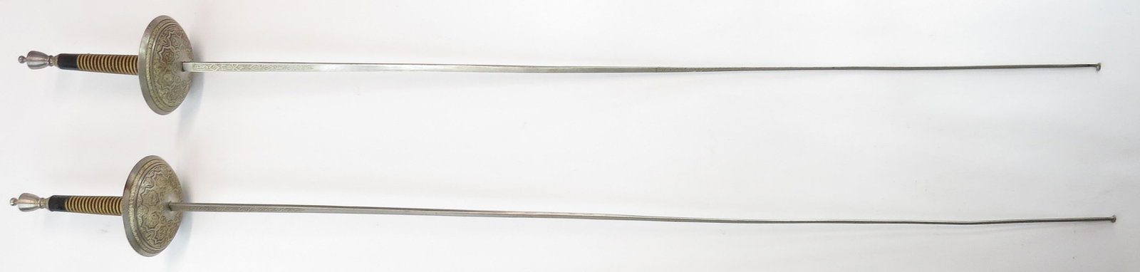 A PAIR OF SPANISH FENCING FOILS: Elaborately etched and gilded Toledo work, displaying exceptional detail. Corded wooden grips, original blades with forged-in buttons. First half of the 20th century. Overall length of each 108cm. Con