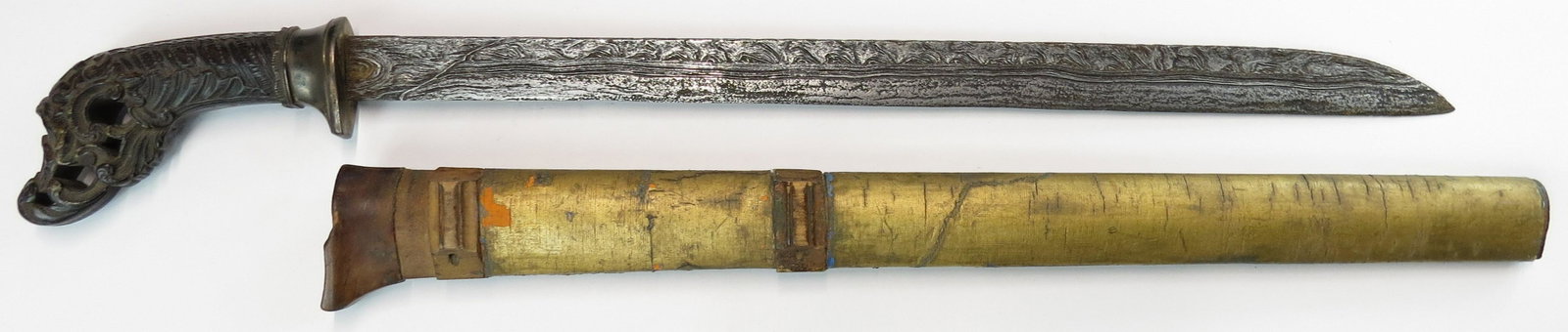 AN INDONESIAN PEDANG SWORD: Sumatran, the horn grip elaborately carved in floral motifs, and modeled ferrule. The single-edged blade of characteristic form forged of very fine pattern-welded damascus steel and deeply etched. In 