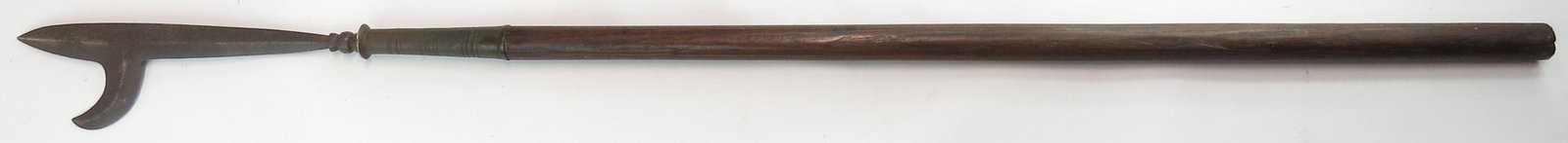 A JAVANESE TOMBAK SPEAR: The well-wrought, blade with lateral hook and profiled base. The brass ferrule finely modeled and ribbed. Retains a portion of its hardwood haft. 17th-18th century. Well worn overall, head pitted. Ove