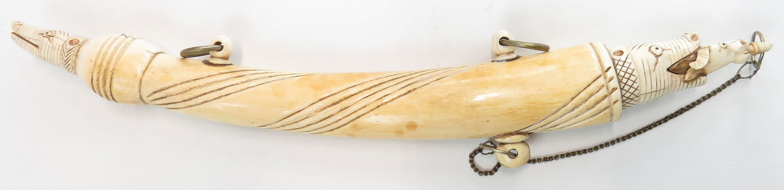 A RARE INDIAN POWDERHORN: Mughal work, a massive example carved of a single large section with applied suspension rings and caps, the main one well-carved in the form of a makara head devouring an ox, the terminal a smaller ma