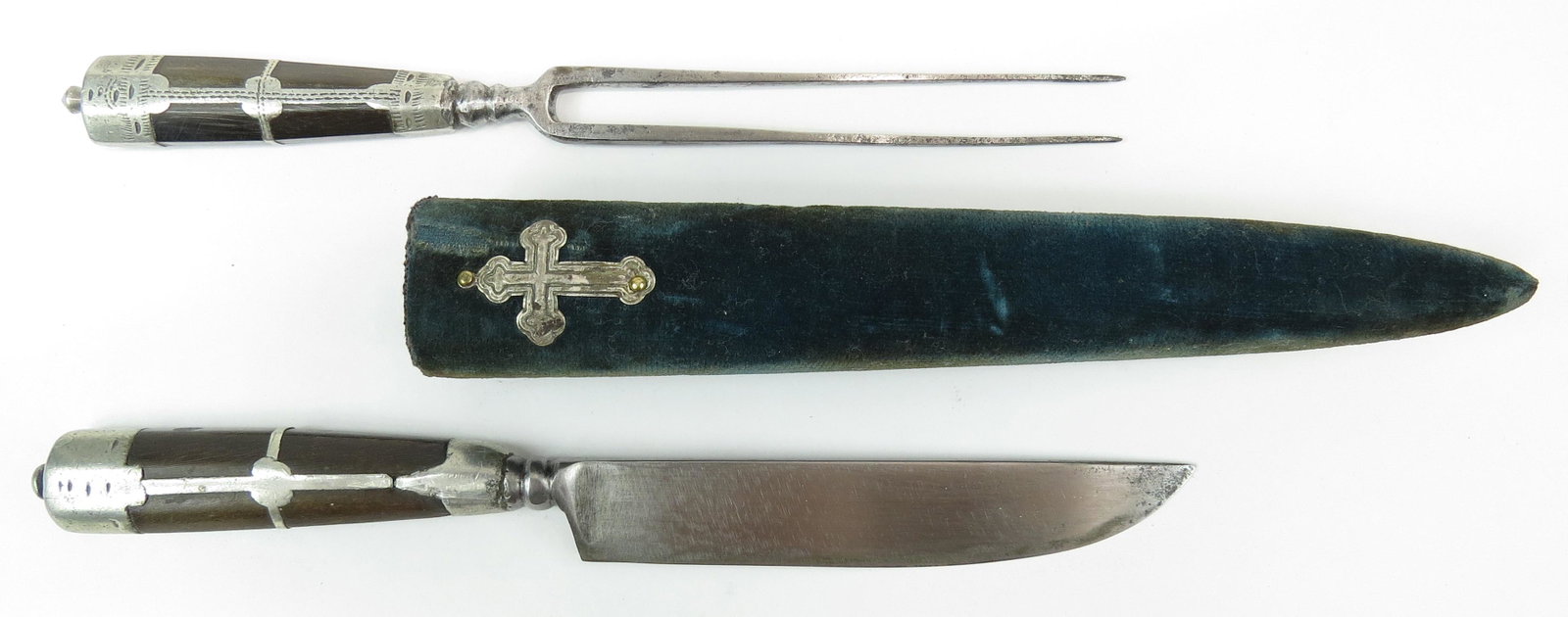 A GREEK REVOLUTIONARY WAR-ERA TROUSSE: Comprising a knife with maker’s mark and two-tined fork, the horn grips with engraved silver mounts. In their wooden scabbard covered with blue velvet, set with a silver cross. Early19th century. Li
