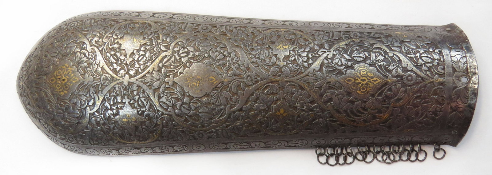 A PERSIAN BAZUBAND ARMGUARD ARMOR: Early Qajar Dynasty, raised from a single plate and finely chiseled overall in flowering vinework with gold embellishments. Early 19th century. Overall length 30.2cm. Condition II