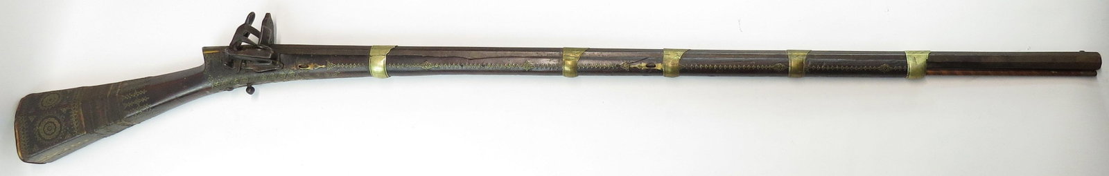 AN OTTOMAN SHISHANA MUSKET: The dark hardwood stock of characteristic form, inlaid with brass studs, horn and bone in complex geometrical motifs. With large miquelet lock and heavy, octagonal barrel retained to the stock by engr