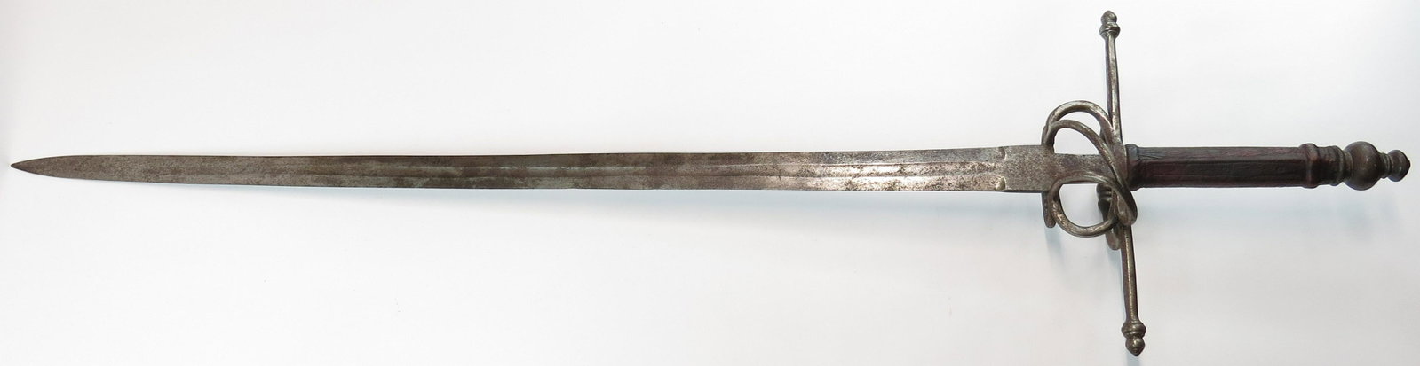 A VICTORIAN-ERA HAND AND A HALF SWORD: A massive example, mounted in steel. With spherical pommel, guard with beaded quillon terminals, complex ring guard, and leather-covered wooden grip. The long, double-edged blade with fine central ful