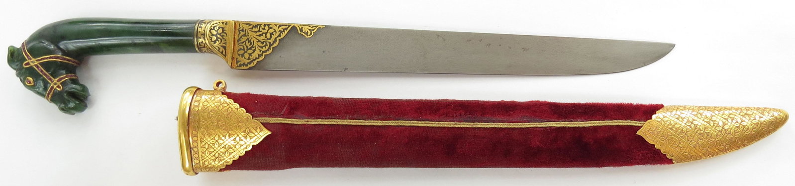 A MUGHAL JADE-HILTED KARD DAGGER: The grip carved of a single piece of deep green jade, terminating in a fully-modeled horses head, the eyes and bridle executed in fine gold and set with rubies and turquoises. The steel bolster finely