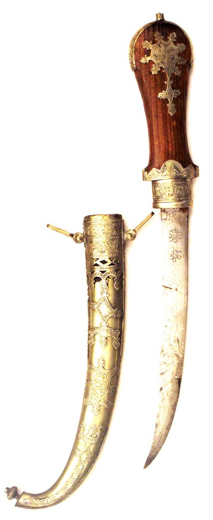 A Moroccan Koumiyya Dagger: The wood grip and scabbard with heavily engraved silver and brass mounts, curved single-edged blade. Late 19th century. 43 cm overall length, blade 22.5 Condition II