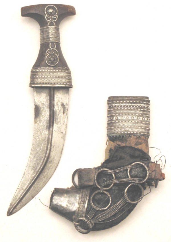An Omani Khanjar Dagger: Of typical form, the flared grip mounted in filigreed silver, the curved, double-edged blade with central rib, wooden scabbard with velvet covering mounted in filigreed silver en suite with the hilt. 