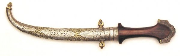 A Moroccan Koumiyya Dagger: Of characteristic form with flared pommel, the wooden grip and scabbard with deeply-engraved silver and brass mounts, with exceptionally fine curved blade with double-edged blade retaining original fi