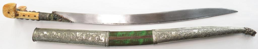 AN OTTOMAN YATAGHAN SWORD: With massive walrus grips of Balkan form, the elaborate tangband and bolsters set with corals. The broad, single-edged recurved blade with narrow. The velvet-covered wooden scabbard with massive embos