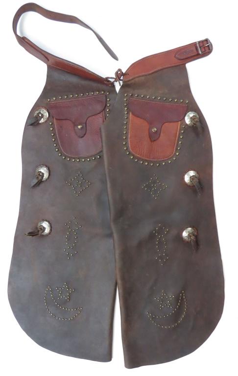 A RARE PAIR OF HEISER CHAPS: A rare pair of oiled leather batwing chaps in deep brown, the belt and patch pockets in a contrasting reddish brown, outlined and embellished with brass studs and set with three conchos on each side.