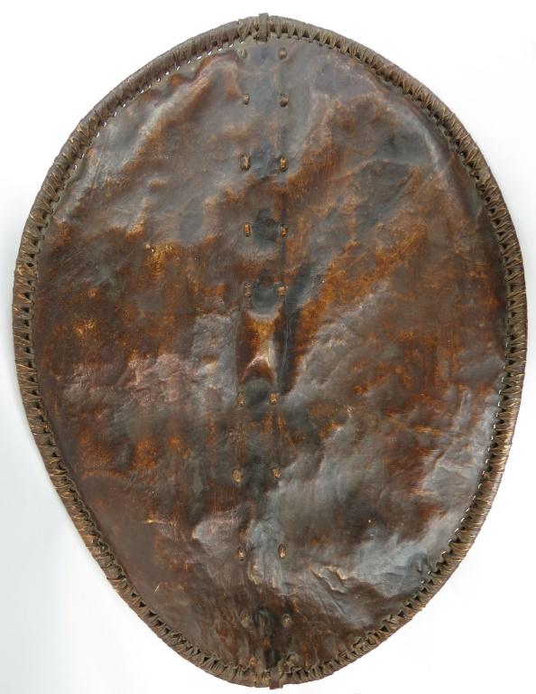 A RARE MAASAI SHIELD: Of an earlier form than typically encountered, made of hide laced to a central wooden post with integral grip, the edges bound to stripped branches with tightly-coiled hide. Mid- 19th century. Overall