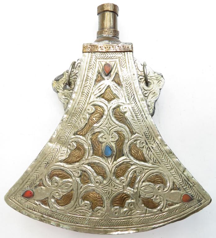 A MOROCCAN POWDER FLASK: A fine example, wrought of brass with pierced and engraved silver decoration with corals to the obverse. Early 20th century. Light wear. Overall length 19cm. Condition II