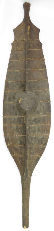 A RARE NIAS SHIELD: Of characteristic form, carved of a single large section of wood, the central boss carved in high relief and a continuous ridge developing into narrow terminals. With integral grip to the reverse and 