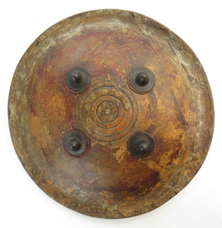 AN INDIAN DHAL SHIELD: A buckler of hardened hide with rolled edge, the central panel with polychroming and four profiled bronze bosses. First half of the 19th century. Worn, losses to colors. Diameter 40cm. Condition III