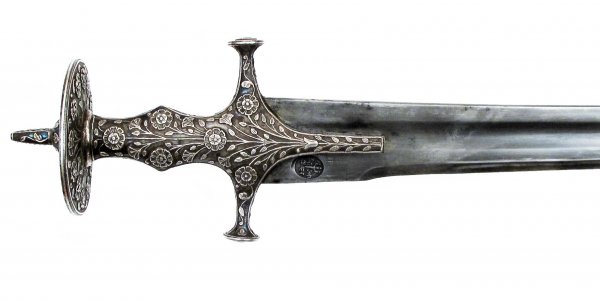 AN INDIAN SABER TULWAR: A large example, the hilt of Udaipur form, of silver sculpted in flowering vine patterns overall and retaining considerable traces of a fine blue pigmentation. The long, single-edged blade with shallo