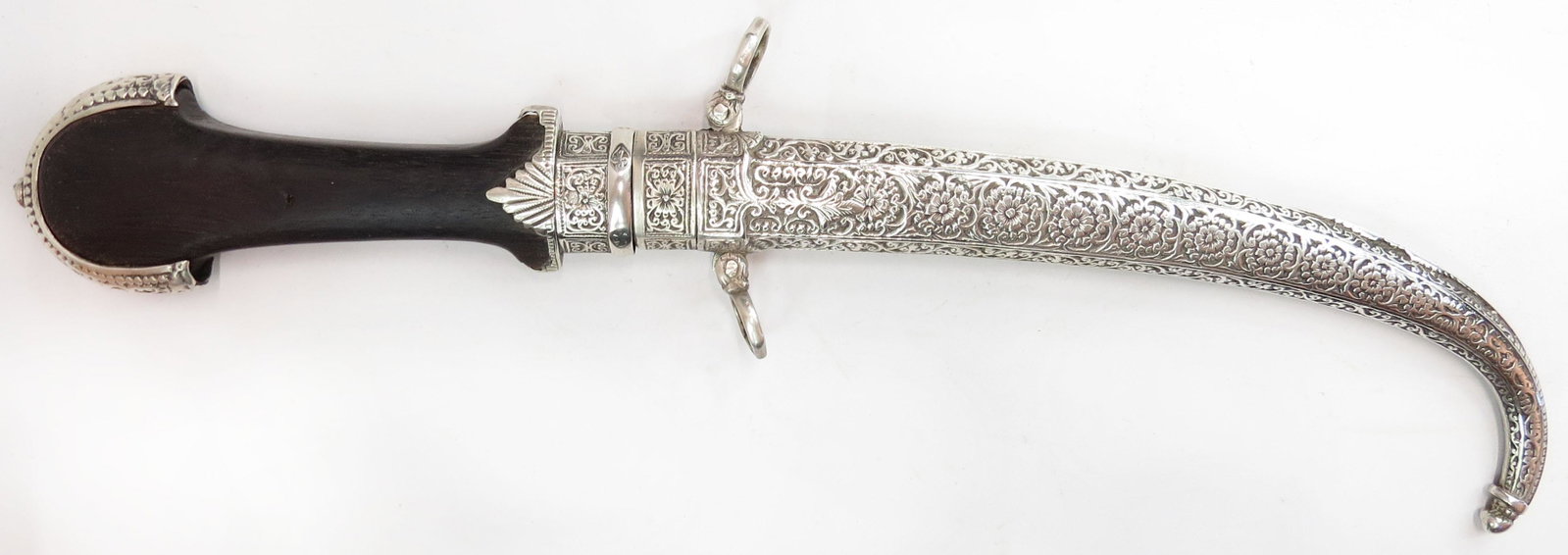 A MOROCCAN KOUMYA DAGGER: A fine example, the elaborately crested pommel and ferrule of silver, the scabbard likewise wrought of silver finely engraved overall, with curved, single-edged blade and polished wooden grip. Latter 