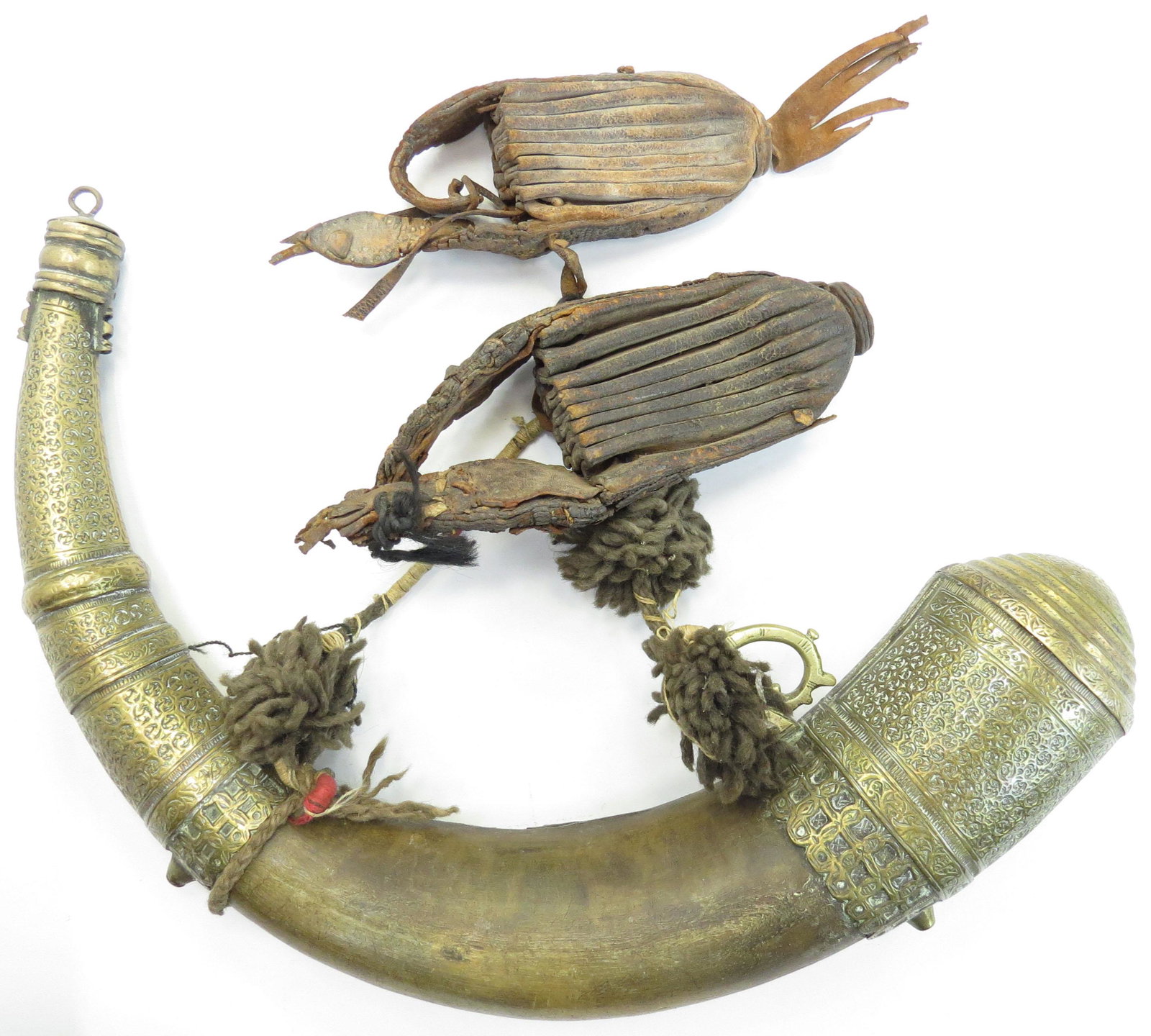 A MOROCCAN POWDERHORN AND BULLET BAGS: The horn body with fine brass mounts elaborately engraved overall with complex vinework, retains its rare very suspension cord with pair of pleated leather bullet bags intact. 19th century. Lacking on