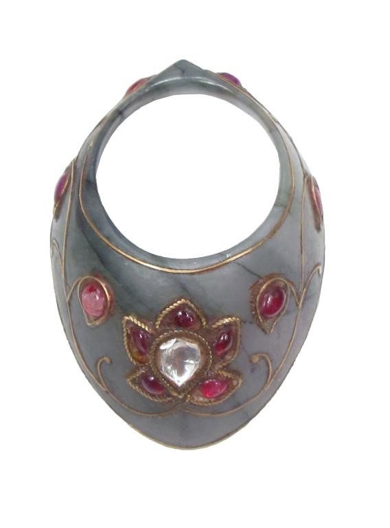A FINE MUGHAL ARCHER’S RING: Of characteristic form, well carved of a single large section of black-veined green jade and set with 11 cabochon rubies and a large faceted center stone, likely white sapphire or diamond. Each stone 