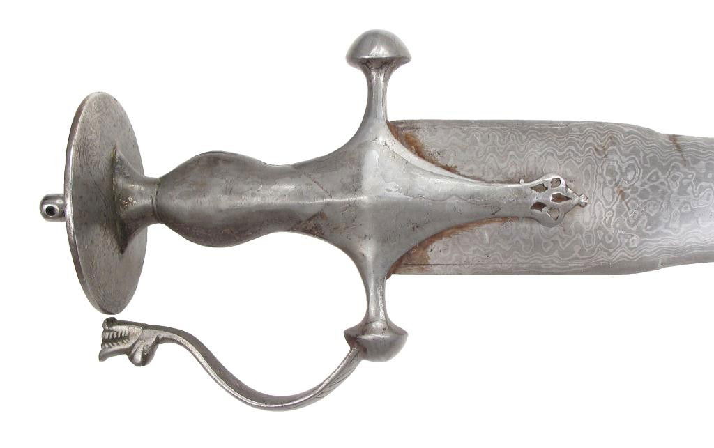 AN INDIAN TULWAR SWORD: The iron hilt with knucklebow terminating in a dragon’s head, the broad, straight, double-edged blade forged of active pattern-welded damascus steel. Mid-18th century. Light wear. Overall length 77.