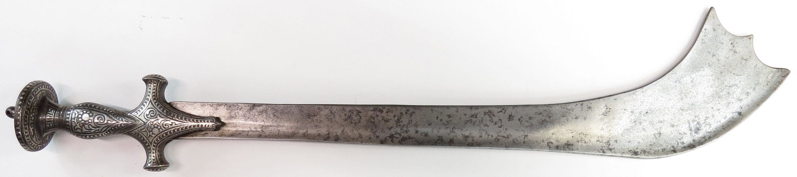 A NEPALESE KORA SWORD: With heavy blade of traditional elephant ear form, with T-back and fullered spine, the tip scrolled. Indian hilt of steel with fine and intricate silver inlay work overall. Late 18th- early 19th centu