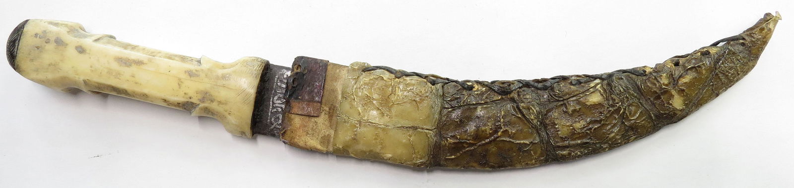 A SUDANESE DAGGER: The polished bone grip with flared pommel and bolsters, the curved, double-edged blade etched overall with Arabic calligraphy. In its albino crocodile sheath. Late 19th century. Minor wear. Overall le