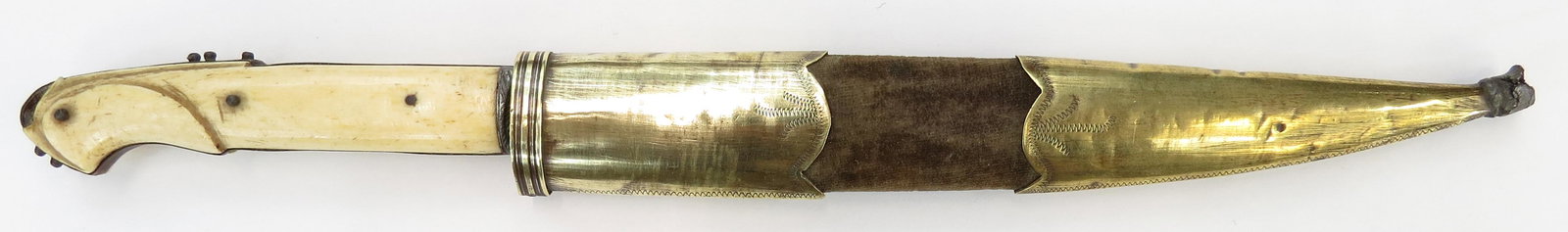 A BOSNIAN DAGGER: The bone grips with beaked pommel, the tang studded. Broad, single-edged blade inscribed in Arabic characters. In its velvet-covered wooden sheath with brass mounts with incised borders. Minor wear, g