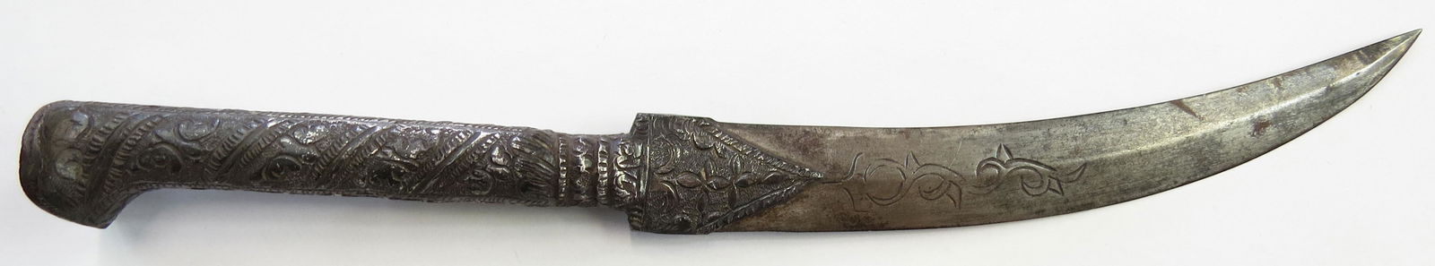A BALKAN DAGGER: The characteristic silvered grip with spiral bands of decoration, the blade curved, with central dirge and engraved vinework. Latter 19th century. Age-darkened. Overall length 30.5cm. Condition II