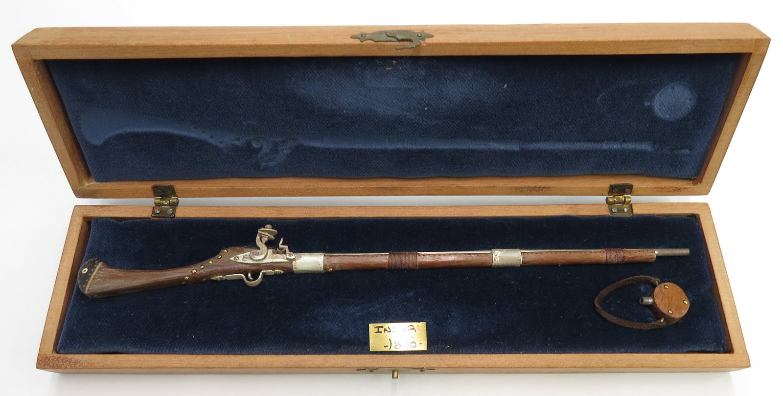 A MINIATURE INDIAN FLINTLOCK MUSKET BY EDUARDO RUIZ: A miniature Indian flintlock musket made entirely by hand, the stock carved of hardwood with flint mechanism, barrel, triggerguard and bands all superbly detailed. With characteristic powder flask. In