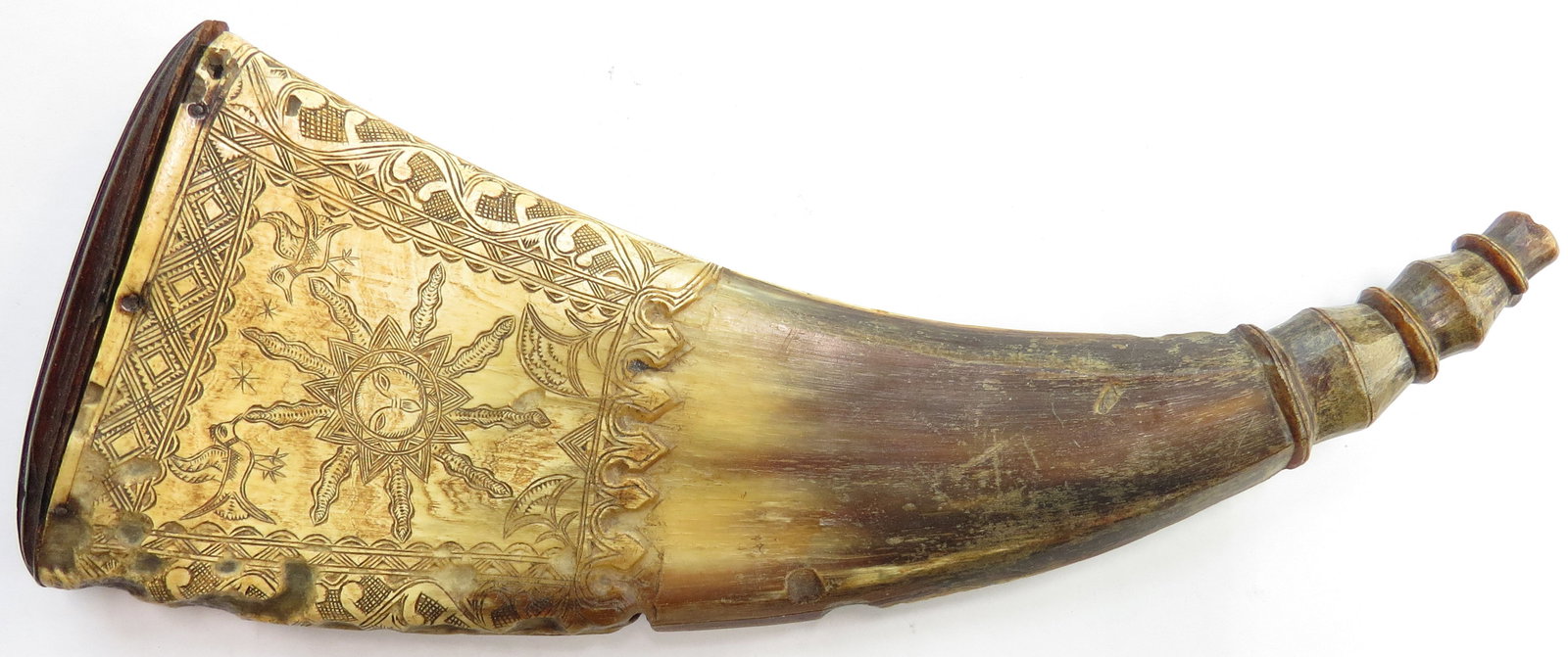 A RARE SPANISH COLONIAL POWDERHORN: Of blond-brown pressed horn with fluted cap, superbly carved with a sun in splendor bordered by stars, birds and flowers to one side and a moon surrounded by flowering vines and a distinctive 10-point