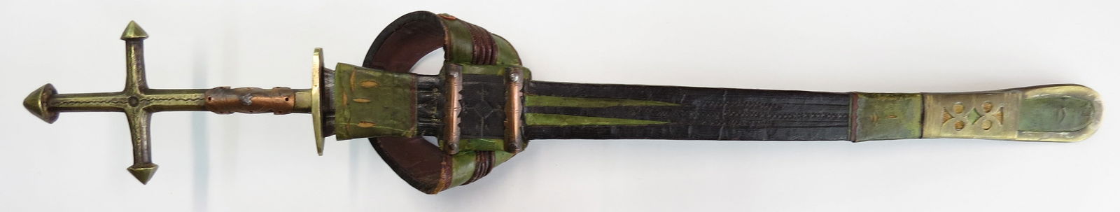A TUAREG TELEK ARM DAGGER: Of characteristic form, the brass mounts with cruciform pommel, the scabbard pierced and engraved, with characteristic armband, steel blade. First half of the 19th century. Worn. Overall length 52.5cm