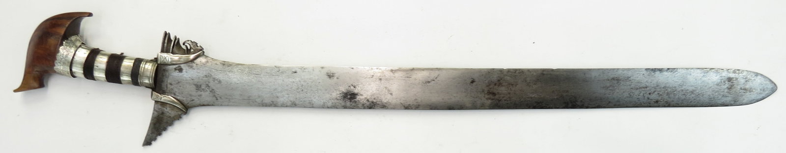 A MORO DATUS KRIS SWORD: The wooden grip with polished banati wood jungayyan pommel with silver mounts, the uppermost with okkir decoration, and fiber wrap. Handforged broad, straight blade with separate ganga showing faint p