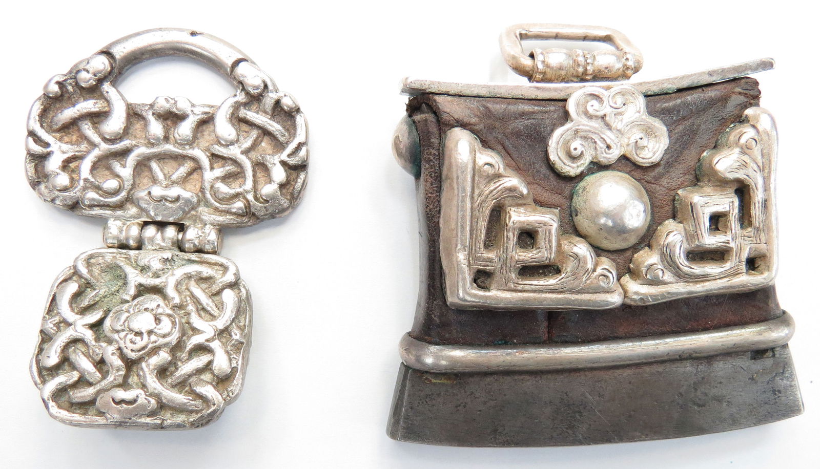 TWO RARE MONGOLIAN BELT MOUNTS: Comprising a pair, a sword- or dagger suspension band and chukmuk or fire-striker/ tinder pouch. Each massive, with cast and embellished silver mounts, the suspension band hinged, the chukmuk retainin