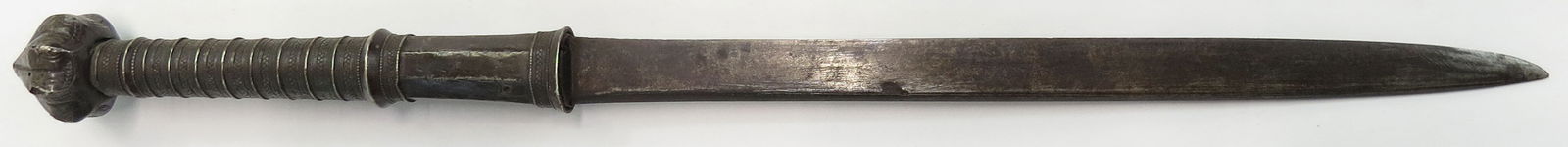 A BURMESE DHA DAGGER: Mounted entirely in silver, the long grip with large pommel of faceted lotus-bud form, with banded grip and faceted ferrule, the blade well-wrought. Latter 19th century. Age darkened. Overall length 4