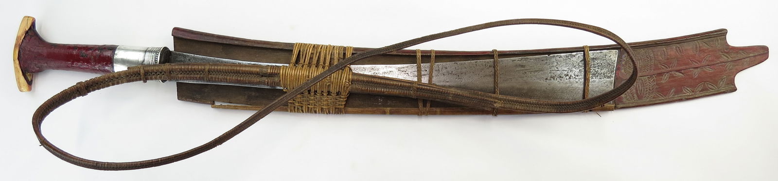 A KACHIN NAGA HEADHUNTER DAO SWORD: Kachin work, the hilt with applied bone pommel, the grip wrapped with braided and lacquered rattan with silver ferrule. The stout, chisel-edged blade with characteristic flared tip, with layer-forged