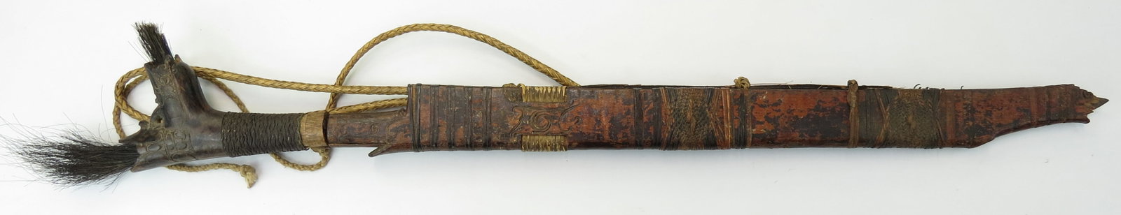 A DAYAK HEADHUNTER PARANG IHLANG OR MANDAU SWORD: The grip of ironwood, finely-carved with aso motifs and retaining its intricately-woven wrap and hair ornaments. The handforged blade with expanded tip chisel-edged and convex on the reverse. In its c