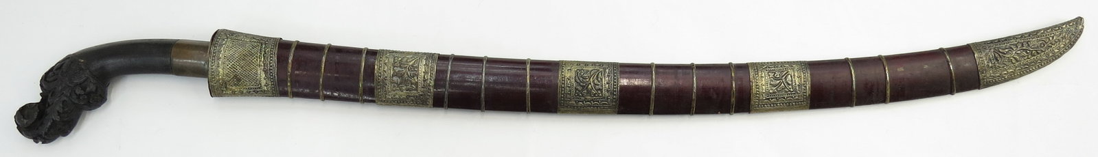 A SUMTRAN PARANG SWORD: Elaborately carved horn handle with brass ferrule, and well-wrought steel blade of characteristic form with double fullers at the spine, possibly damascus steel, and inlaid with YA MUHAMMAD! (O Muhamm
