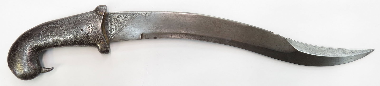 AN INDIAN ZIRA BOUK DAGGER: Of massive proportions, the iron grip terminating in a parrot head and inlaid in silver flowering vine motifs. The broad blade recurved, with silver inlay to forte and chamfered edge with pronounced a