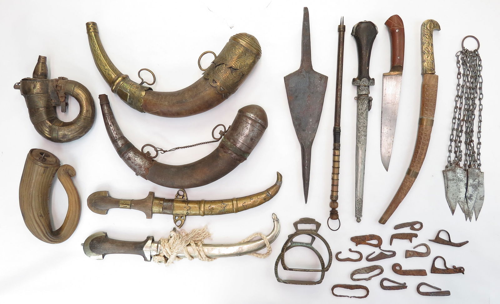 A LOT OF 16 ASSORTED ARMS AND RELATED ITEMS: Comprising 2 Moroccan powderhorns, 2 moroccan daggers, 2 powderhorns, a pair of stirrups, a harpoon head, a Moroccan genoui dagger, a Turkish knife, an Algerian knife, a chain weapon, 13 ancient flint