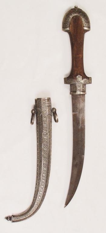 A MOROCCAN KOUMIYYAH DAGGER: Of characteristic form with flared wooden grip, the arched pommel and scabbard wrought entirely of silver and finely engraved overall. The curved blade with central ridge .Late 19th –early 20th cent