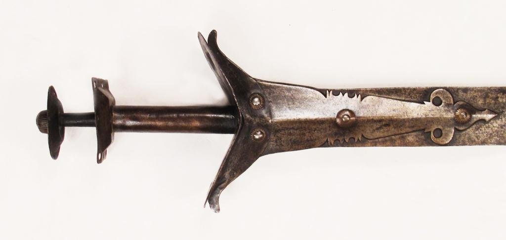 A SOUTH INDIAN NAYAR SWORD: A massive example, rarely encountered. The Old Indian-type hilt composed of iron and brass with broad guard and flared pommel, and long, pierced reinforces at the fort. The graceful blade displays com