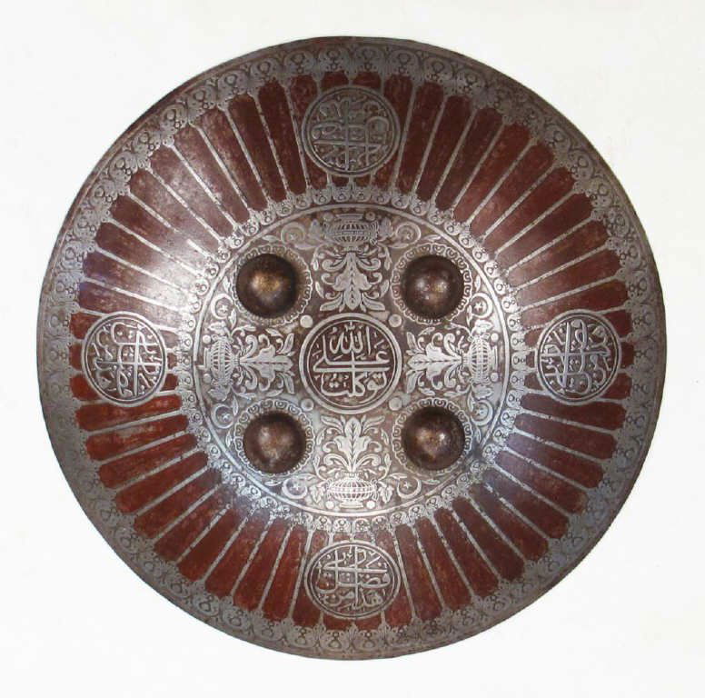 AN OTTOMAN KALKAN SHIELD: A rare example, wrought in steel and superbly chiseled at the center in flowering vines issuing from vases, together with five circular cartouches, the central one inscribed ALLAH, ALI, TUKLAT! The pe