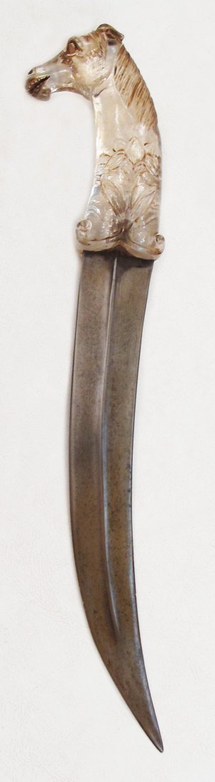 A MUGHAL ROCK CRYSTAL-HILTED KHANJAR DAGGER: Very finely carved, the pommel terminating in a fully-modeled horse’s head. The curved, double-edged blade with central ridge, forged of silver-gray wootzdamascus steel. Second half of the 18th cent